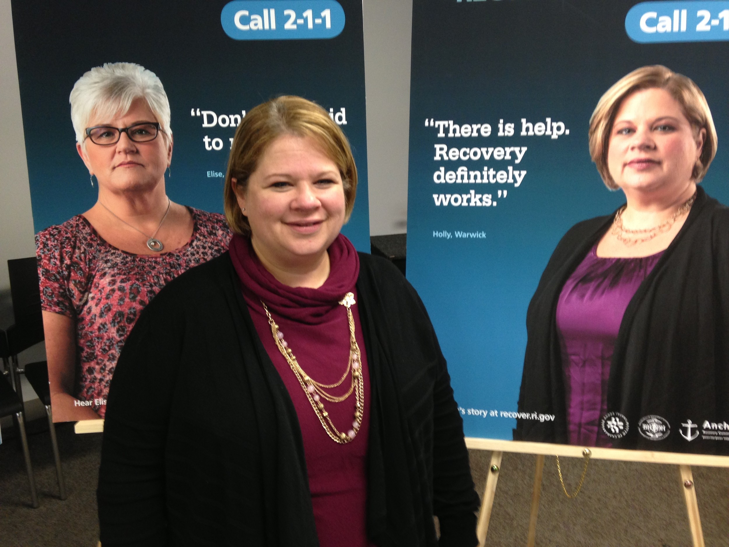 Holly Cekala, executive director of RICares, in front of a poster featuring her story as part of a new media campaign promoting recovery in Rhode Island, following a news conference to launch the campaign.